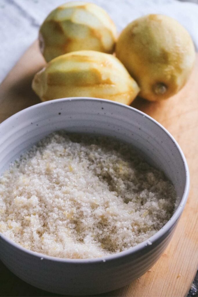 a white bowl filled with a lemon sugar mixture on a cutting board in front of zested lemons.