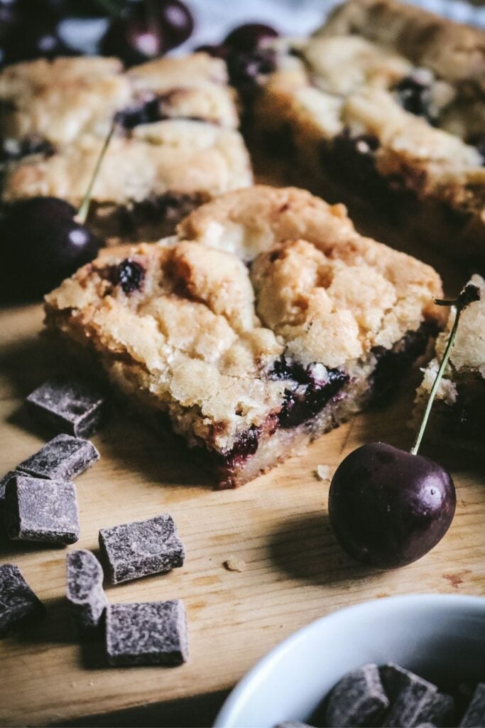 chewy homemade cherry blondies with fresh black cherries and chocolate chunks displayed on a wooden cutting board.
