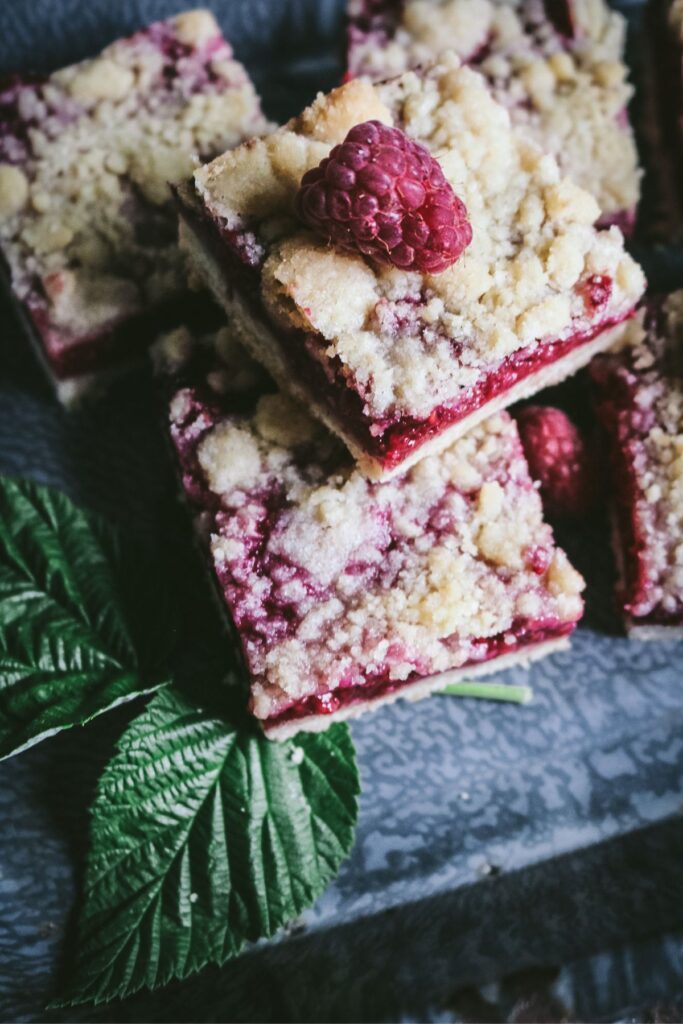 overhead view of fresh raspberry crumb bars in a gray graniteware baking pan with raspberry leaves and a fresh raspberry on top.