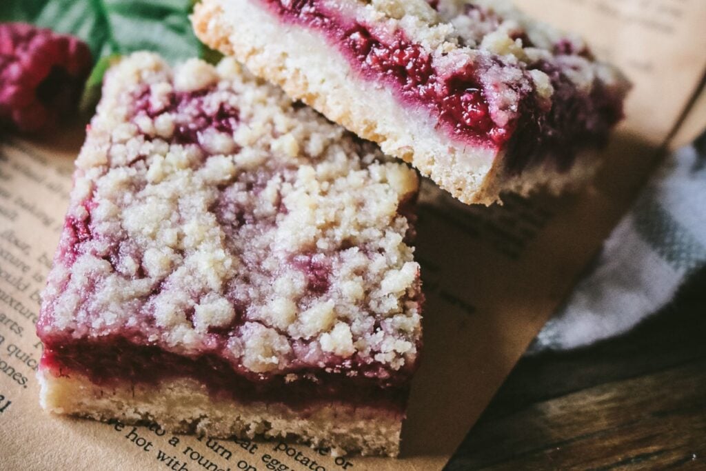 close up view of two buttery raspberry crumb bars with a shortbread crust, lots of raspberries, and a crunchy crumble topping.
