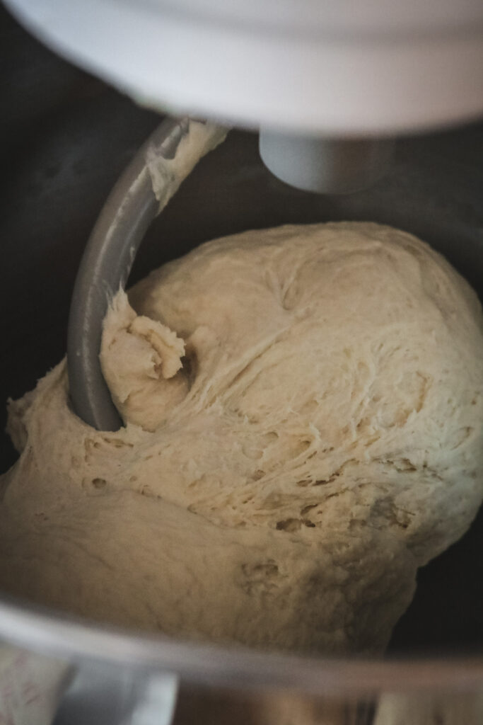 image of dough being mixed with a dough hook in a metal mixing bowl.