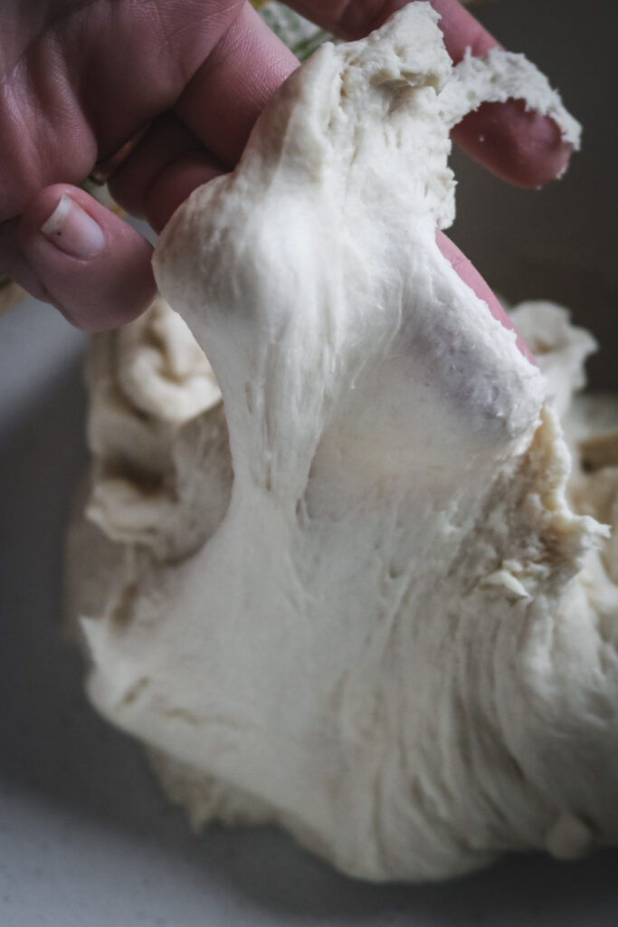 using fingers to stretch bread dough to show gluten development.