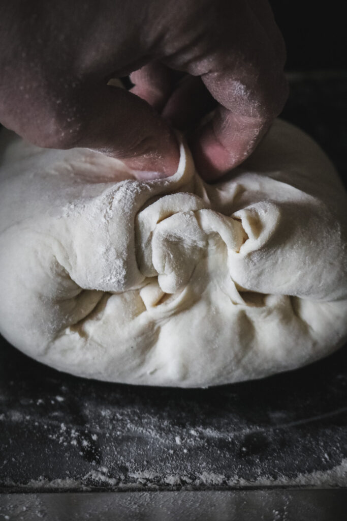 folding the sides of a rolled bread dough log together as part of shaping sandwich bread.