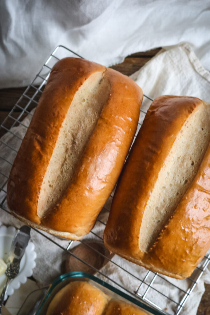 overhead view of two gorgeous golden bread sandwich bread loaves cooling on a wire rack before slicing.