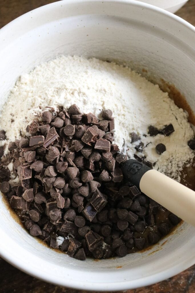 overhead view of a white mixing bowl with the dry ingredients and chocolate chips added to brown butter cookie dough.