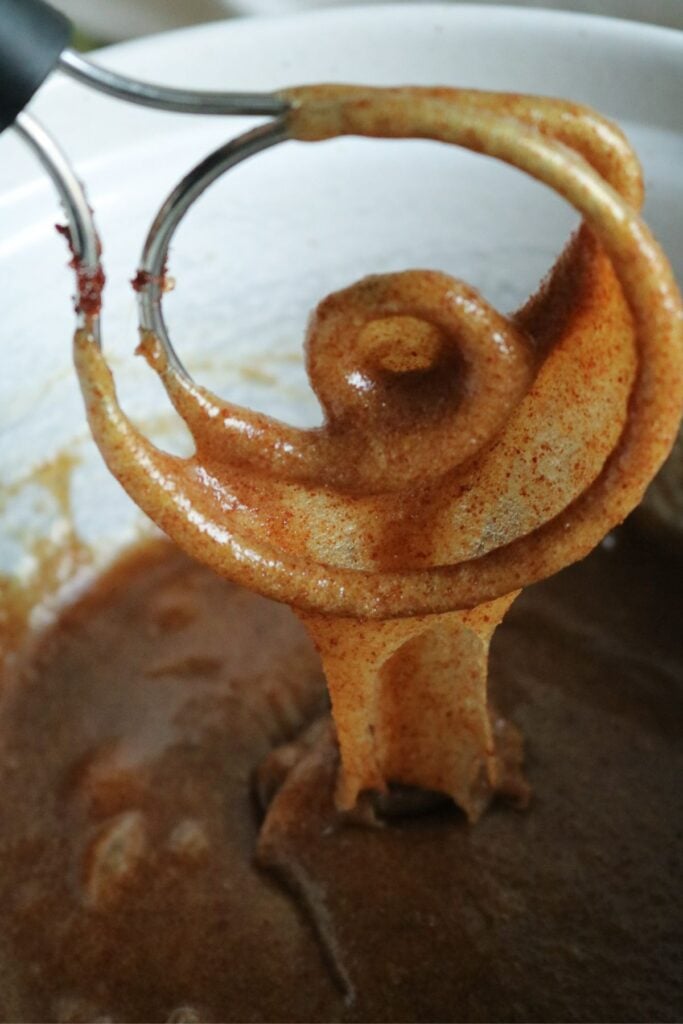 close up view of a dough whisk dripping brown butter, sugar, eggs, and vanilla before adding the dry ingredients.