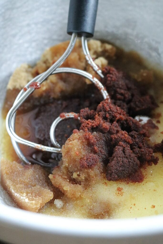 close up view of brown sugar, sugar, and brown butter in a mixing bowl with a dough whisk.