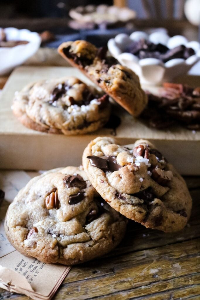 a stack of freshly baked brown butter pecan chocolate cookies on an antique wooden table to highlight the melted chocolate and bits of pecan.