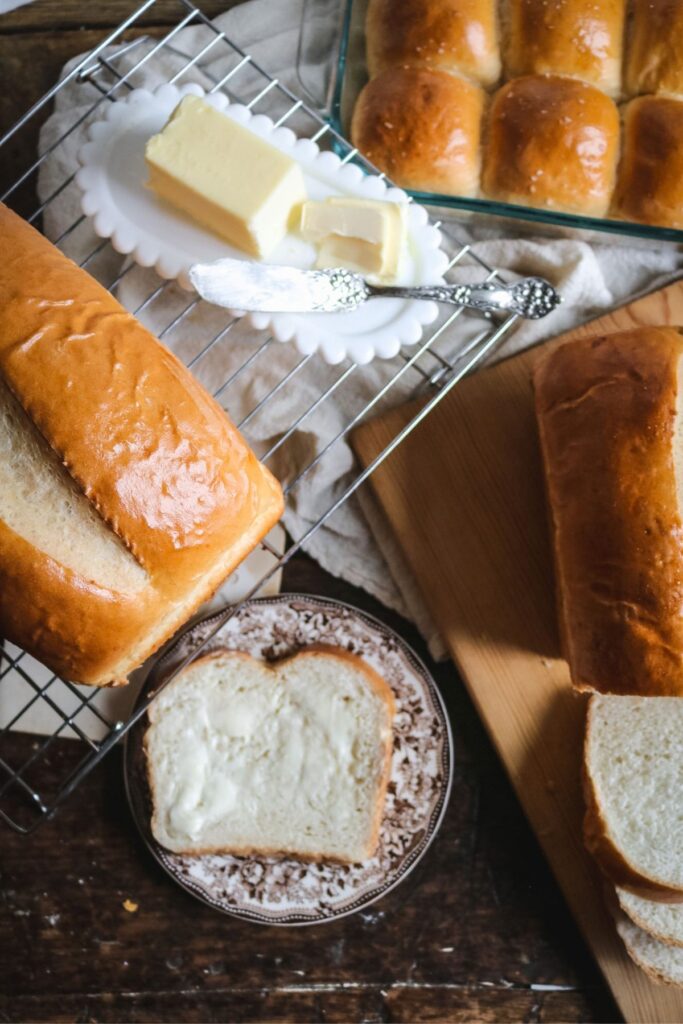 overhead view of a dark wooden table set with freshly baked homemade sandwich bread sliced and served with butter.