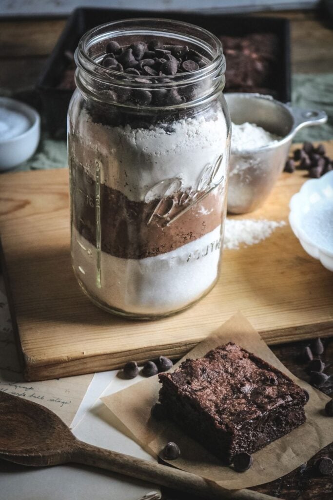 a quart jar of homemade brownie mix behind a thick piece of freshly baked brownie.