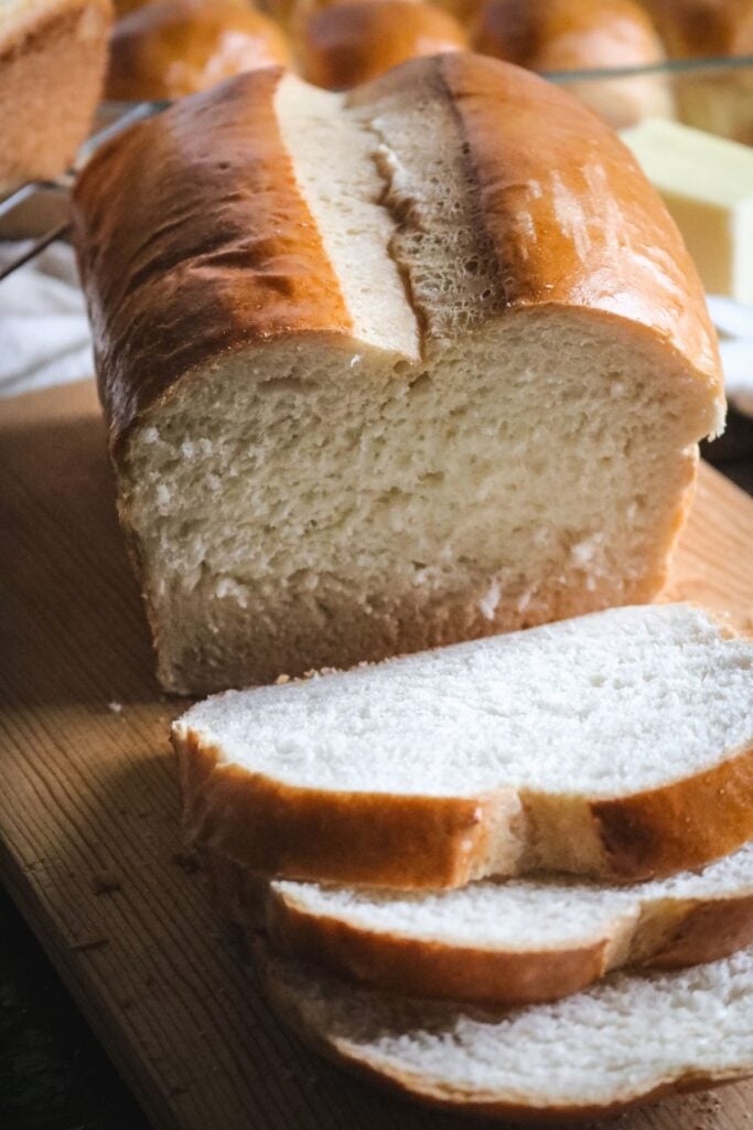 close up view of a loaf of homemade white sandwich bread sliced into slices on a wooden cutting board to highlight its golden brown color and ultra soft texture.