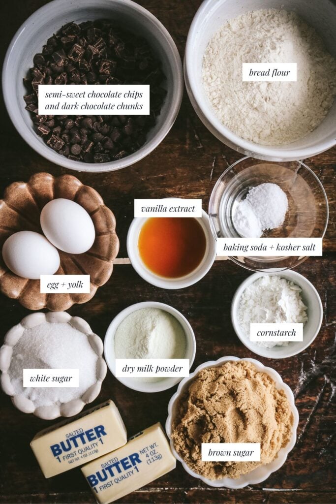 overhead view of an antique wooden table with the ingredients to make brown butter chocolate chip cookies including brown sugar, chocolate chips and chunks, an egg and an egg yolk, and milk powder.