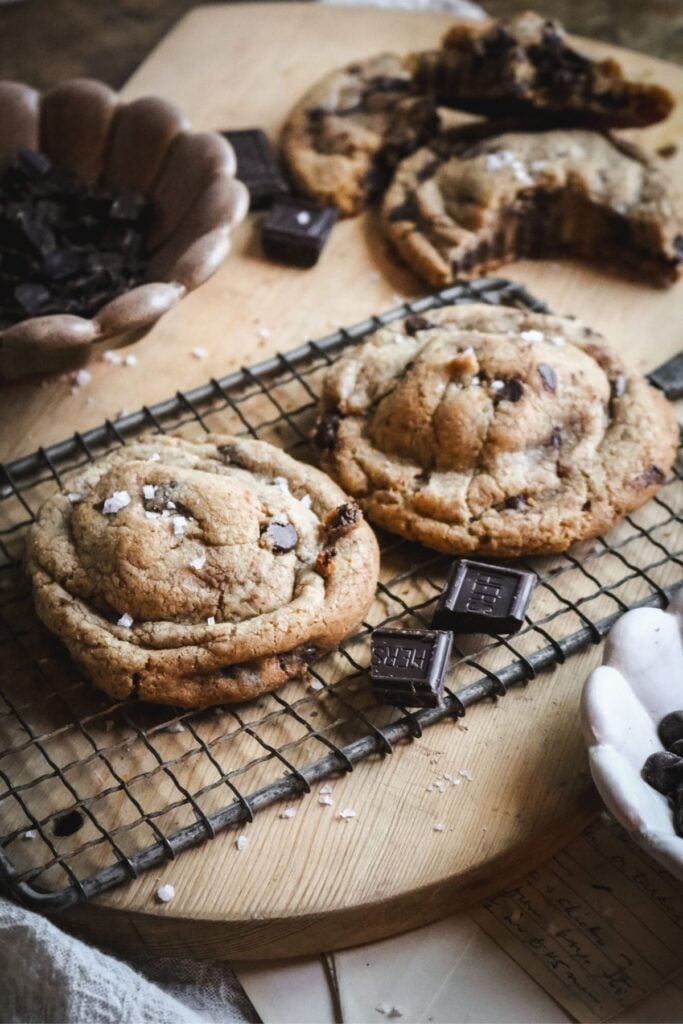 angled view of two large chocolate chip brown butter cookies cooling on a wire rack.