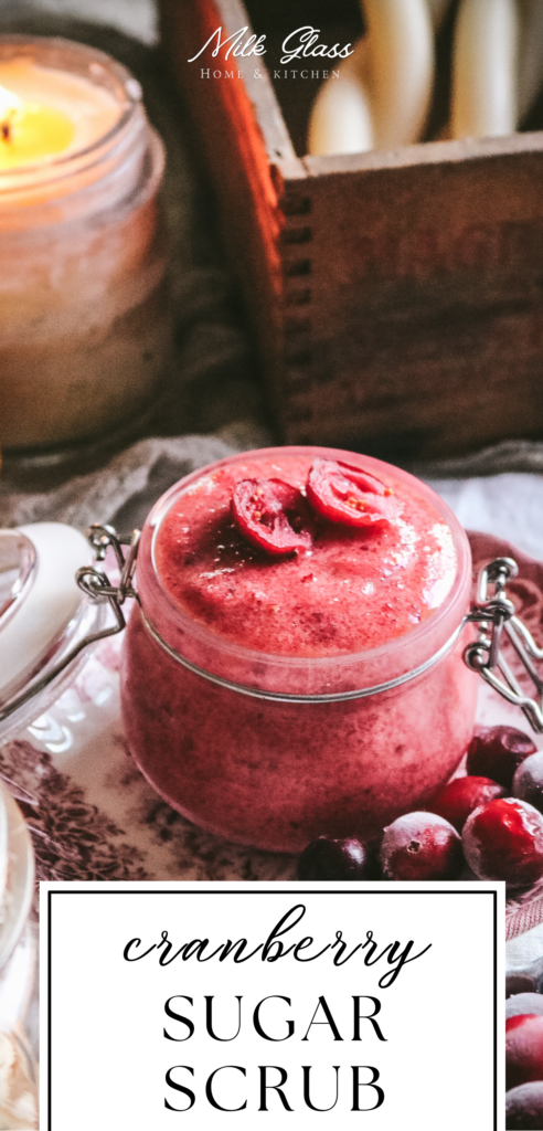pin image with a glass jar of homemade fresh cranberry sugar scrub on a red and white plate next to fresh berries and a candle.