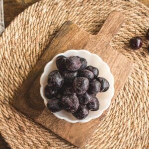 white milk glass bowl full of frozen cherries on a dark wood cutting board.