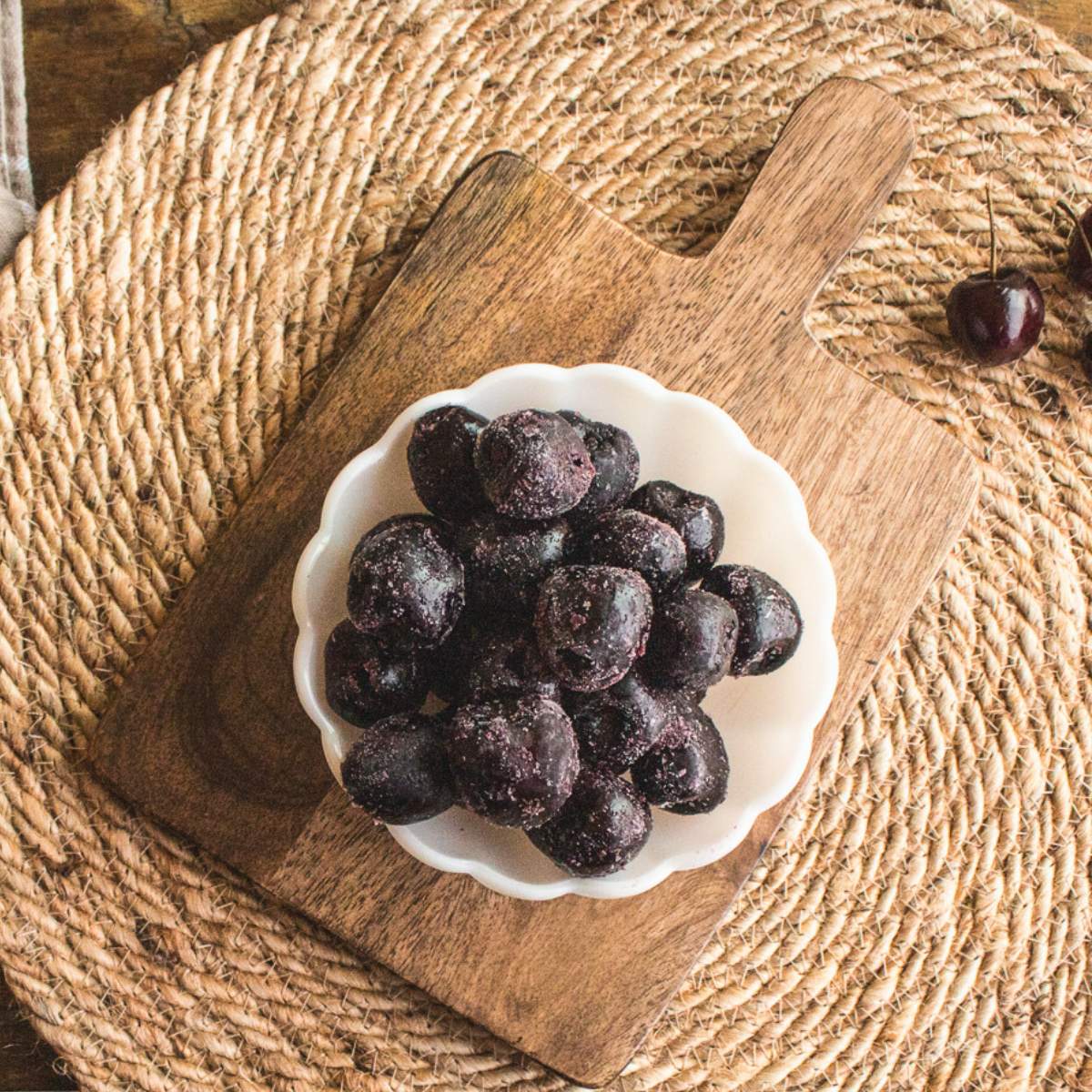 white milk glass bowl full of frozen cherries on a dark wood cutting board.
