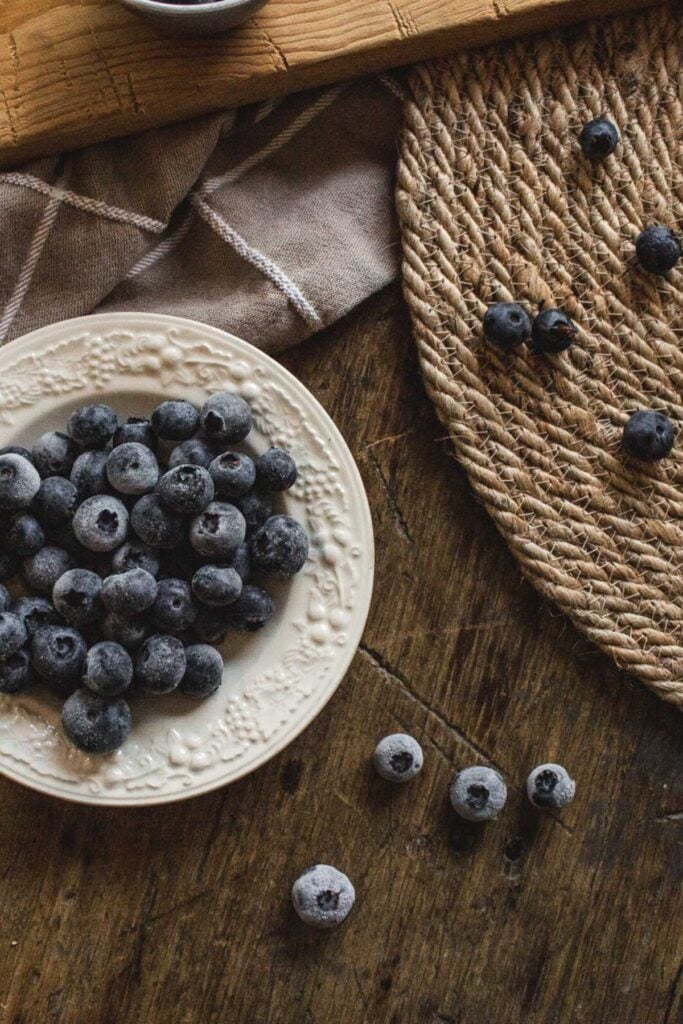 antique bowl with frozen blueberries on a wooden table.