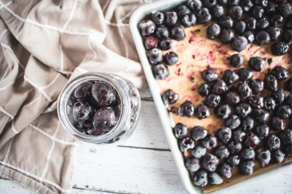 sheet pan with frozen cherries next to a mason jar.