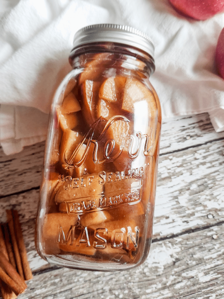 mason jar with homemade apple liqueur recipe on a wooden surface.
