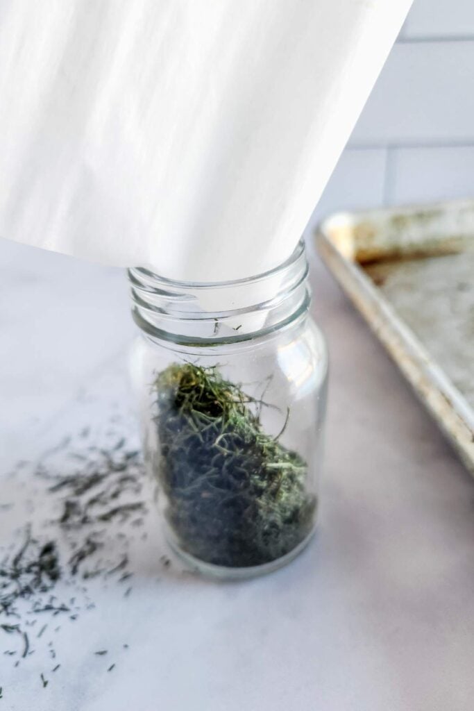 pouring dried dill in a spice jar using parchment paper. 