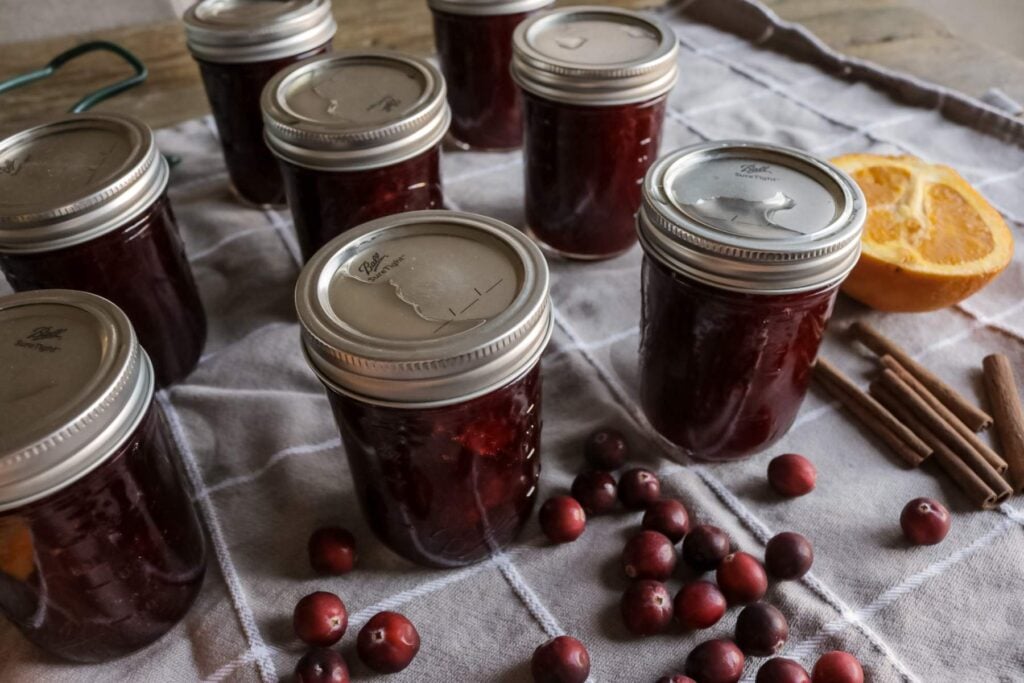 jars of cranberry sauce cooling on a kitchen towel.