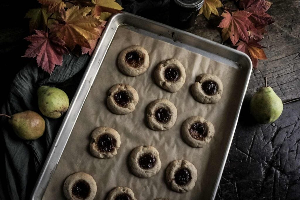 freshly baked pear butter cookies on a sheet pan by fresh pears and leaves.