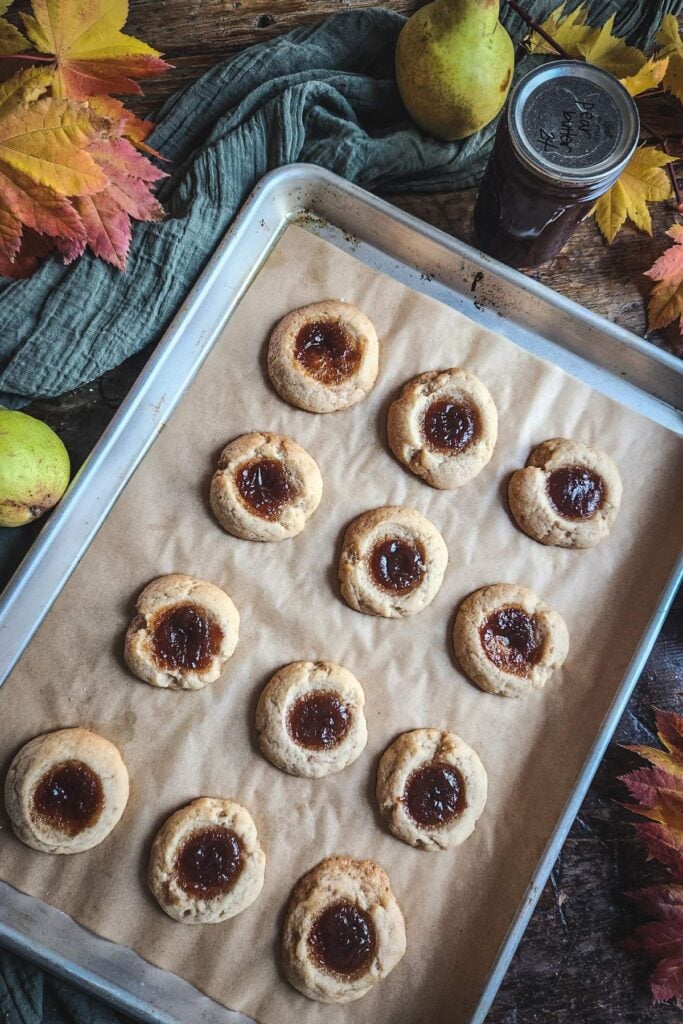 sheet pan with pear butter thumbprint cookies cooling next to pears, pear butter, and leaves.