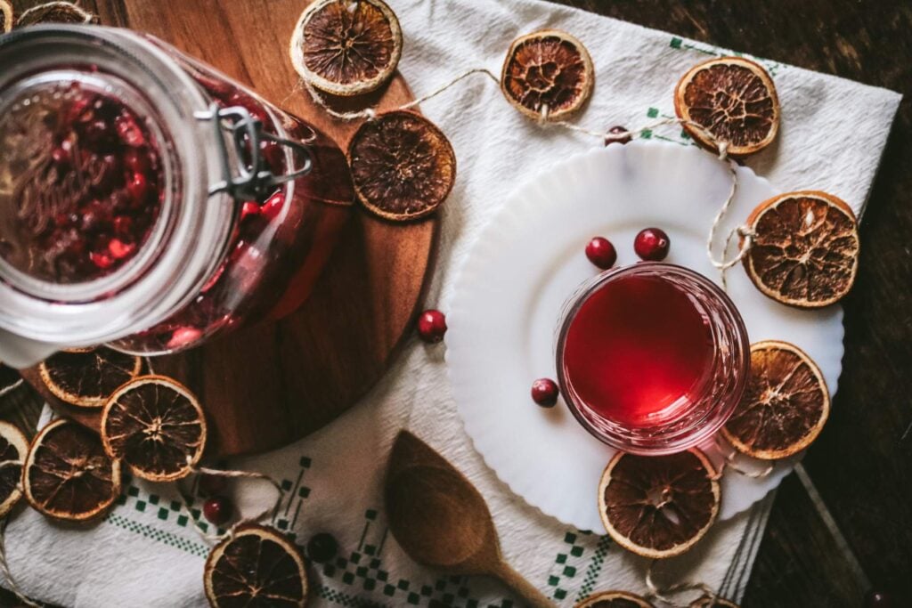 overhead view of a glass with homemade cranberry liqueur next to dried orange slices and fresh cranberries.