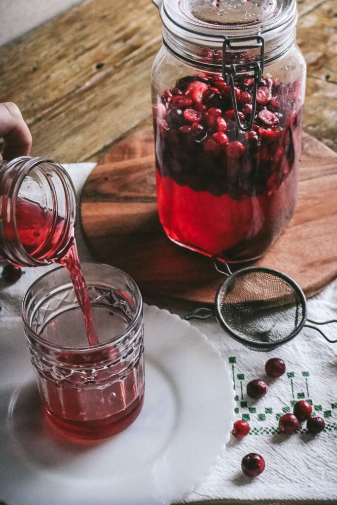 pouring homemade cranberry liqueur into a serving glass.