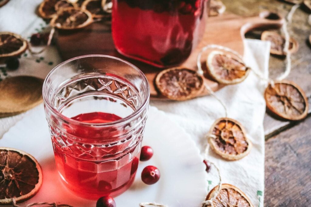 cocktail tumbler with homemade cranberry liqueur next to dried orange slices.