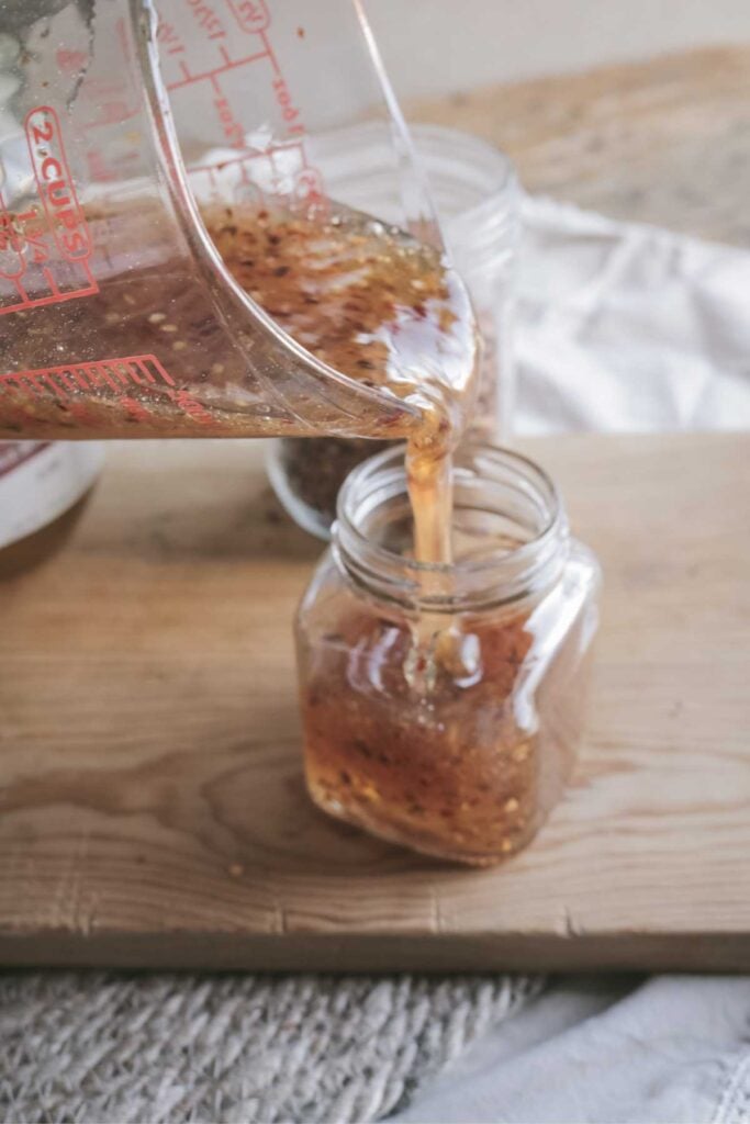 pouring hot honey into a glass jar.
