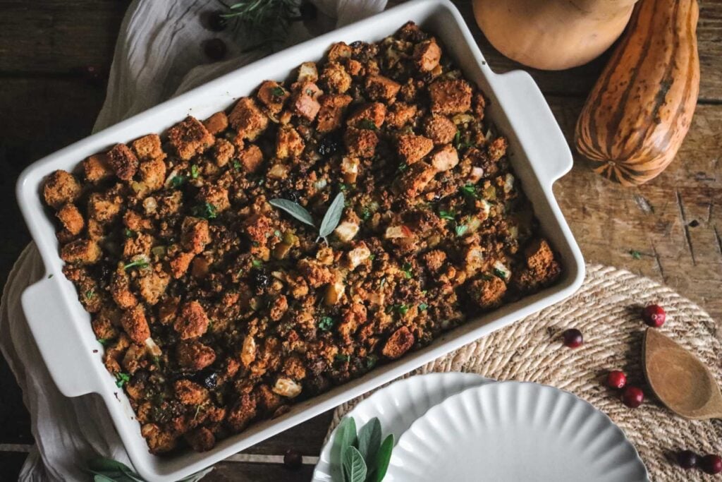 white baking dish with homemade sausage sourdough cornbread stuffing with sage leaves on top.