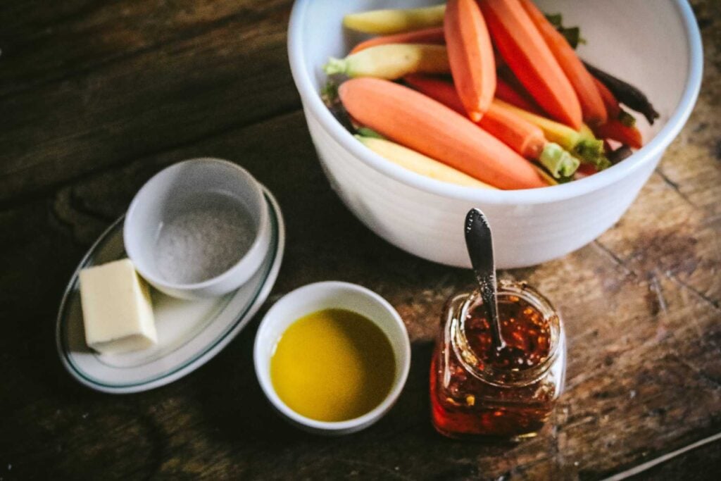 milk glass bowl with peeled rainbow carrots, olive oil, hot honey, salt, and butter.