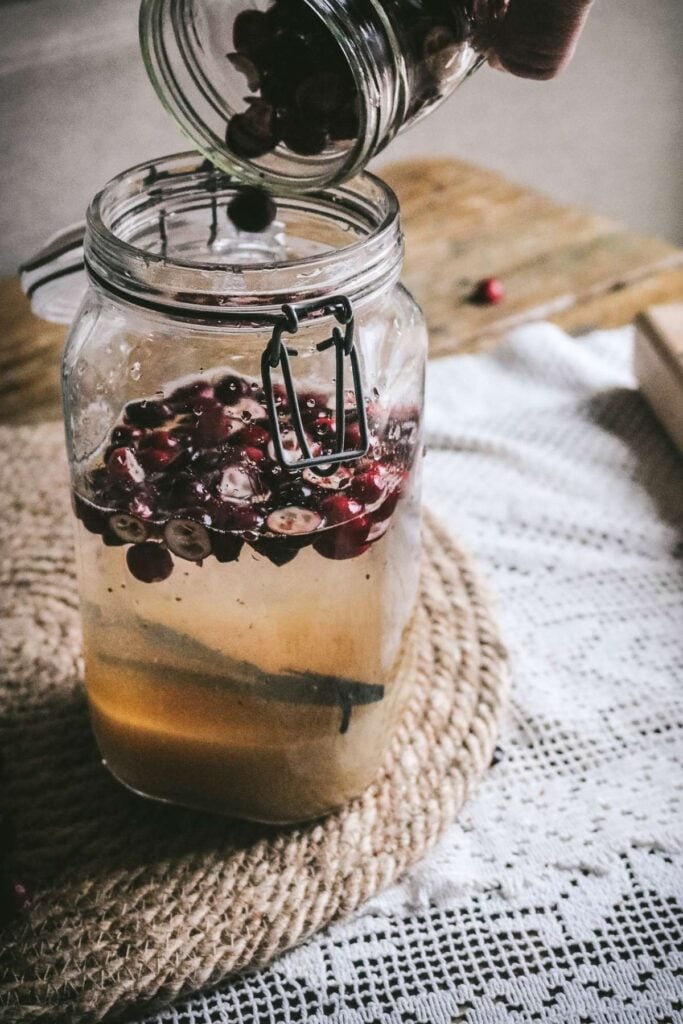 pouring cranberries into a jar of vodka, water, sugar, and vanilla bean.