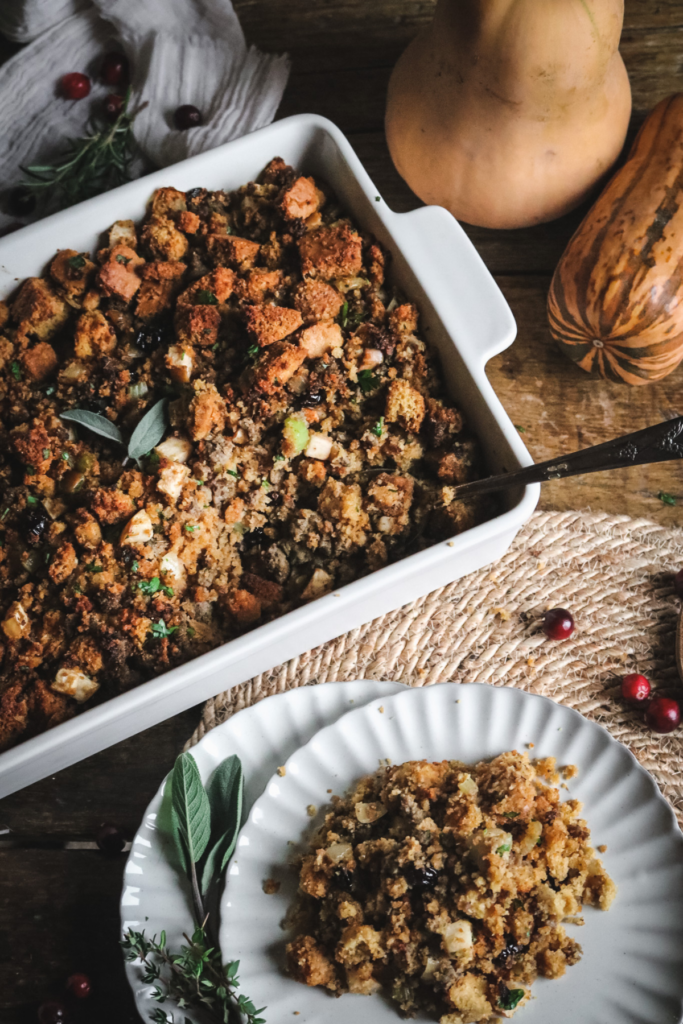 white plate with homemade sourdough cornbread stuffing next to fresh cranberries and sage.