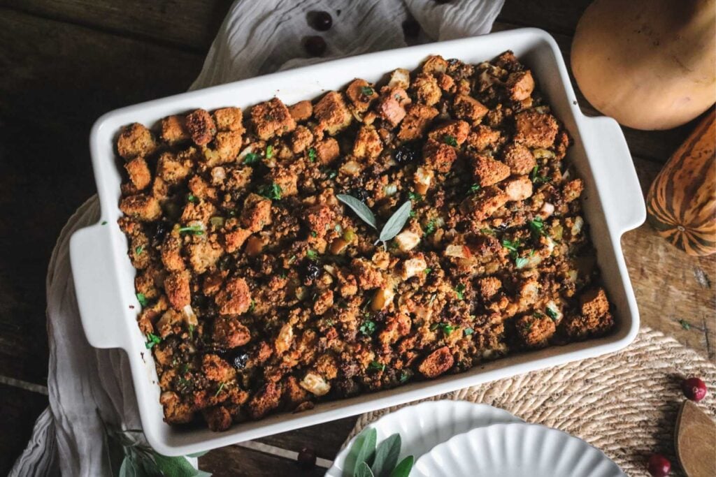 large white baking dish with homemade sourdough cornbread sausage stuffing with fresh sage leaves on top.