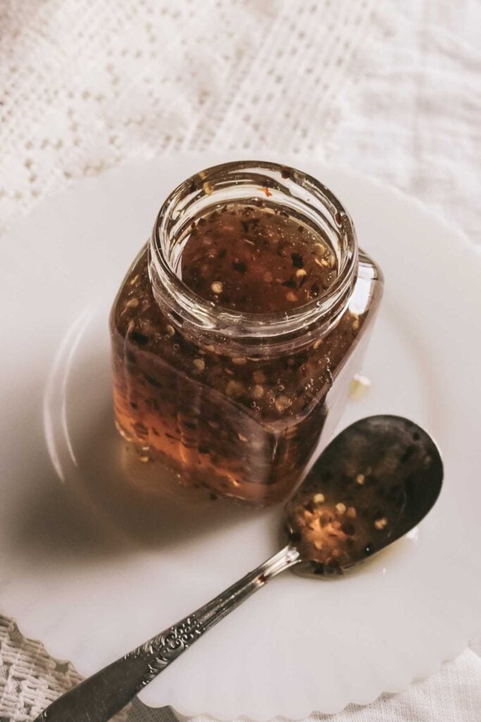glass jar of hot honey next to a spoon on a white plate.