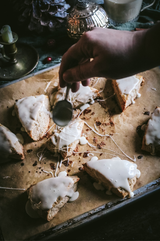 spooning glaze over a tray of eggnog scones.