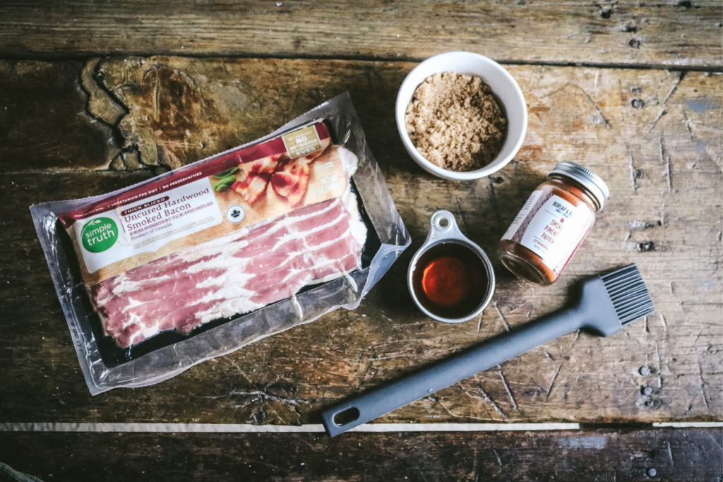 thick cut bacon, maple syrup, brown sugar, and smoked paprika on a wooden surface.