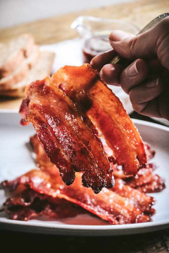 lifting up two slices of maple bacon with a fork.