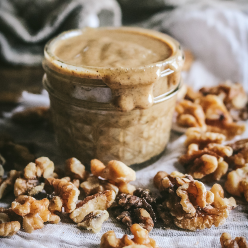 close up view of a jar of creamy walnut butter next to walnuts.
