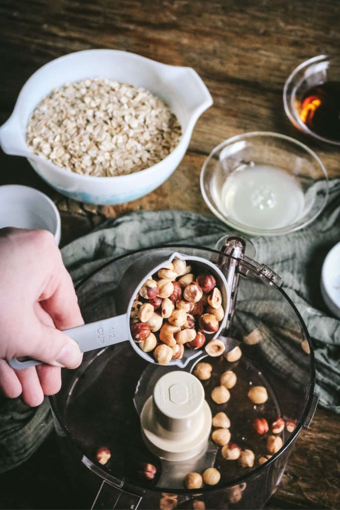 pouring roasted hazelnuts into a food processor.