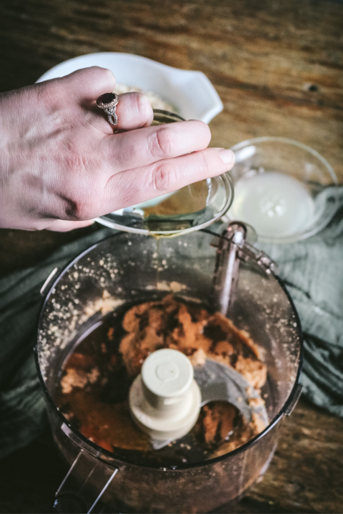 pouring maple syrup over hazelnut butter in food processor.