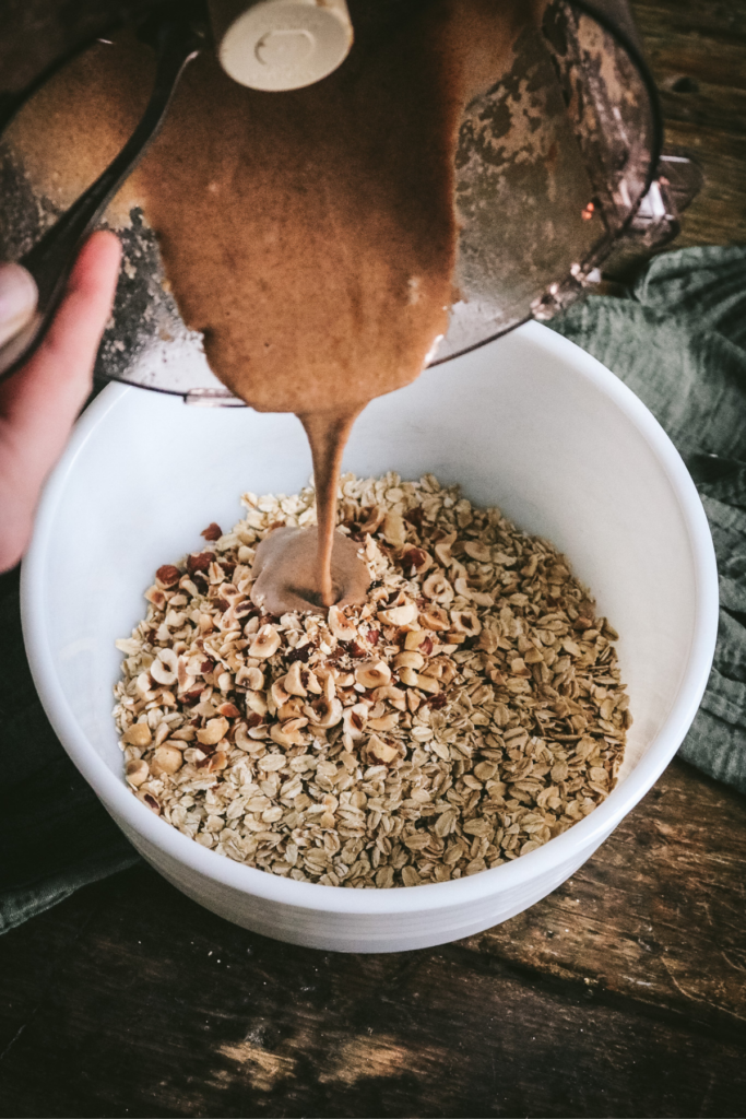 pouring hazelnut butter mixture over oats for granola.
