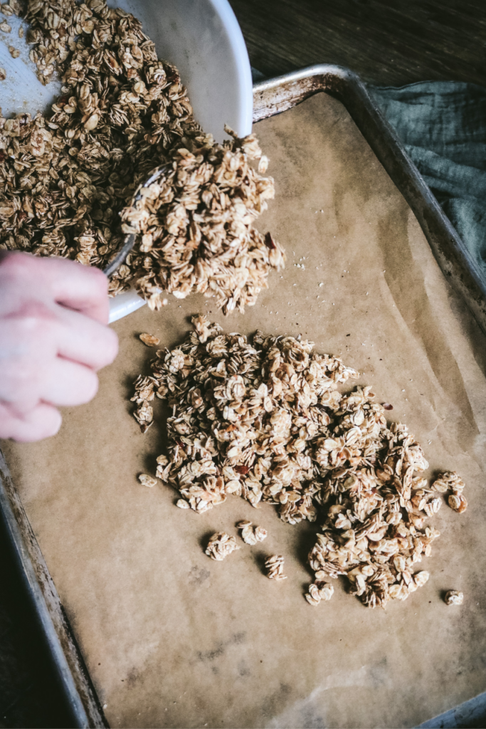 scooping hazelnut granola onto a sheet pan.