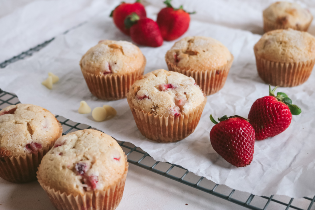 wire rack lined with white parchment paper with strawberry muffins, white chocolate, and fresh strawberries.