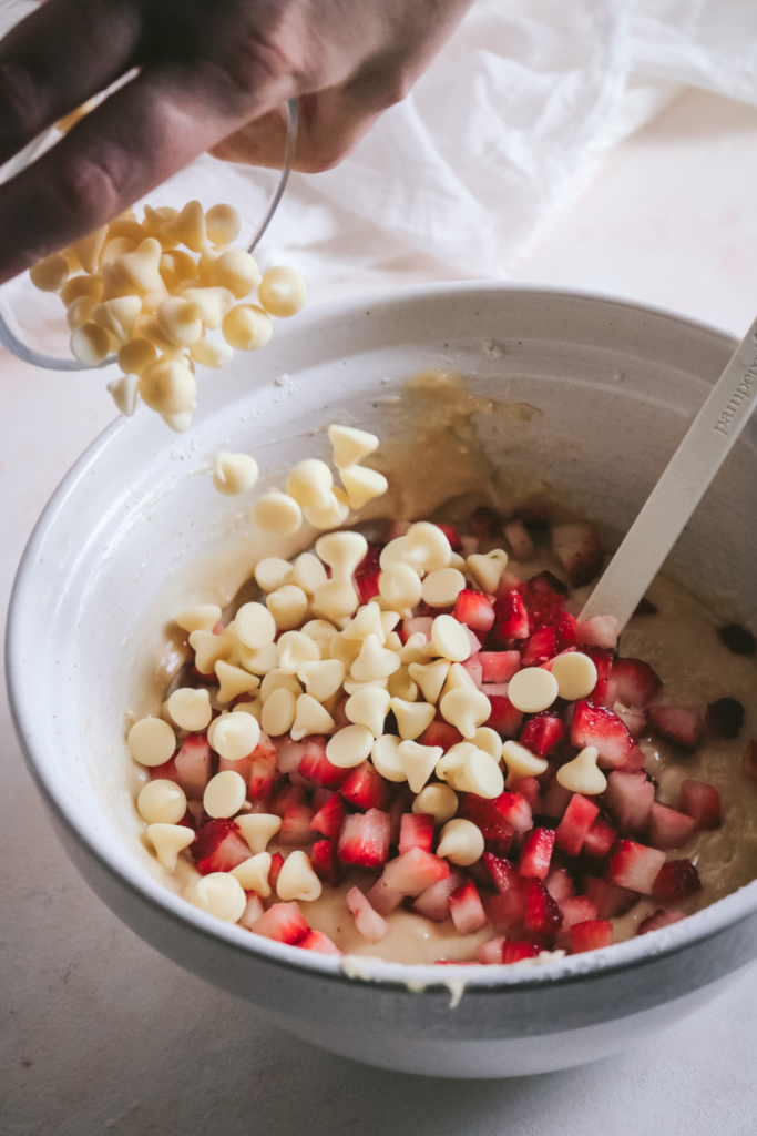 adding white chocolate chips and strawberry pieces to muffin batter.