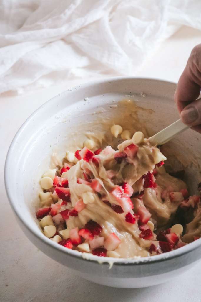 stirring white chocolate chips and strawberries into muffin batter.