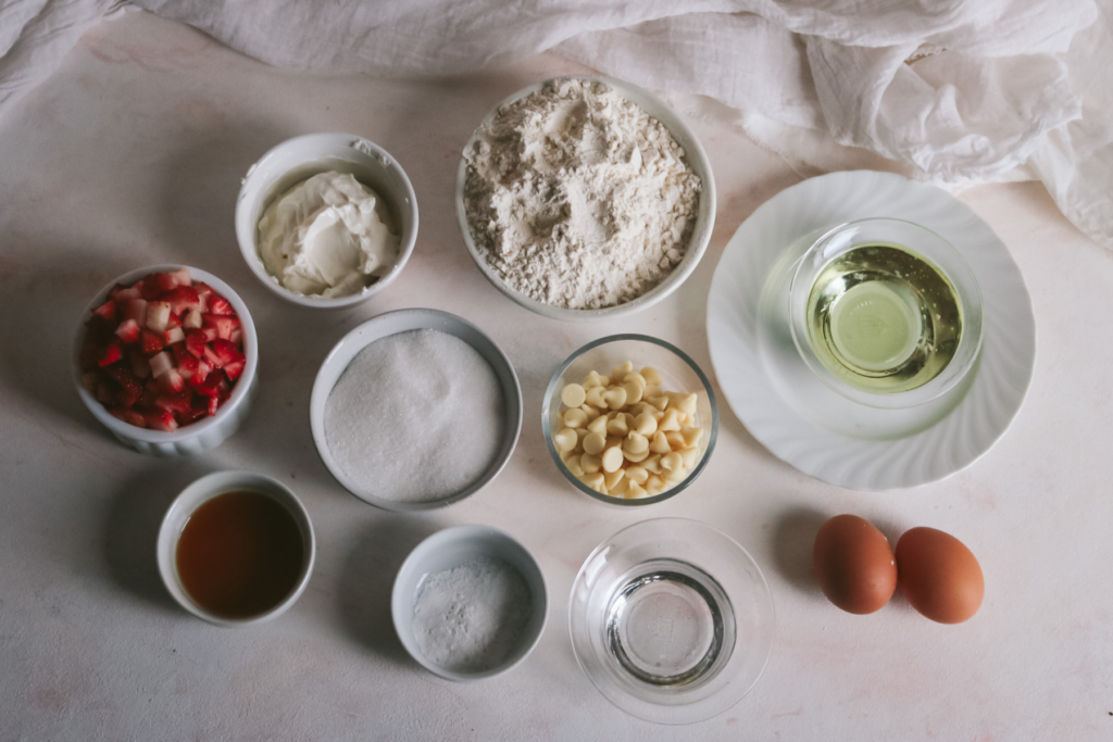 overhead view of the ingredients to make white chocolate strawberry muffins on a pink surface.