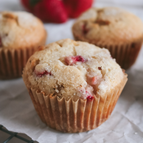 close up of a white chocolate strawberry muffin on a piece of white parchment paper next to fresh strawberries.